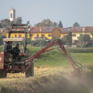 A tractor operates in a rural field with a village backdrop, showcasing rural life and agriculture.