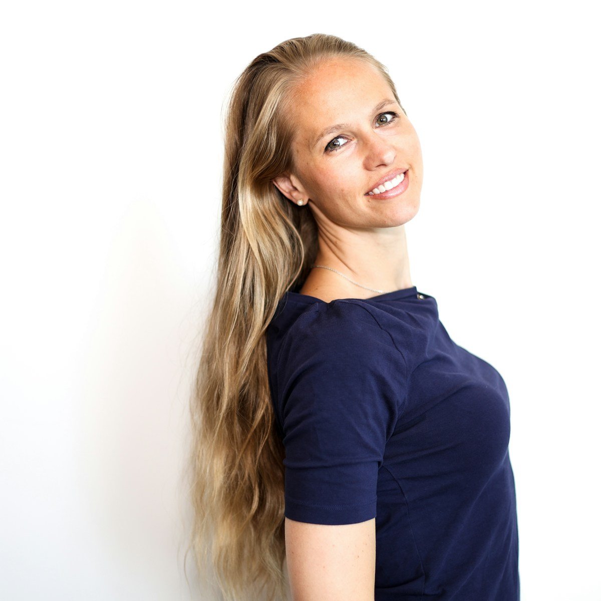 A woman with long hair standing in front of a white wall